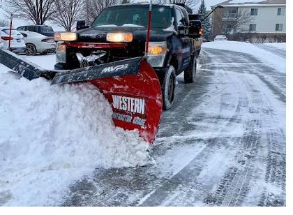 Crew member in high-visibility winter gear operating a snow blower during a storm